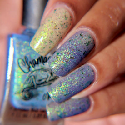The Forgotten Lagoon (UV Polish) by Chamaeleon Nails, flakie UV shifting from pale cream-white on index finger to soft lavender-periwinkle across middle, ring, and pinky in bright daylight, with green-to-orange multichrome flakies, on a light-medium skin tone hand