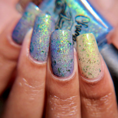 The Forgotten Lagoon (UV Polish) by Chamaeleon Nails, flakie UV contrasting blue-lavender UV-activated fingers against creamy white pinky in bright daylight, with green-teal and orange-shifting ultrachrome flakies, on a light-medium skin tone hand