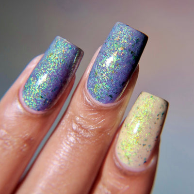 The Forgotten Lagoon (UV Polish) by Chamaeleon Nails, flakie UV mid-shift with two nails in blue-purple UV-activated state and one nail in warm cream resting state, with green-gold iridescent flakes, on a light-medium skin tone hand