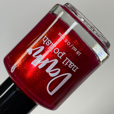 Cup of Cheer by Dam Nail Polish, deep crimson red with fine metallic red-to-orange shifting shimmer, bottle standalone product shot