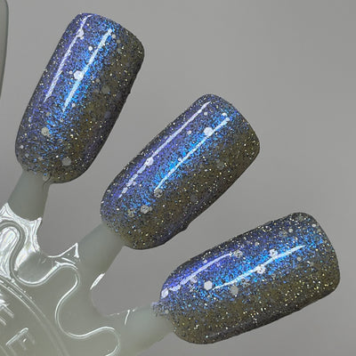 We're Off to See the Blizzard by Dam Nail Polish, deep charcoal-black jelly packed with silver micro-glitter, blue-violet multichrome shimmer streaks, and white hex glitters in studio light, swatch stick
