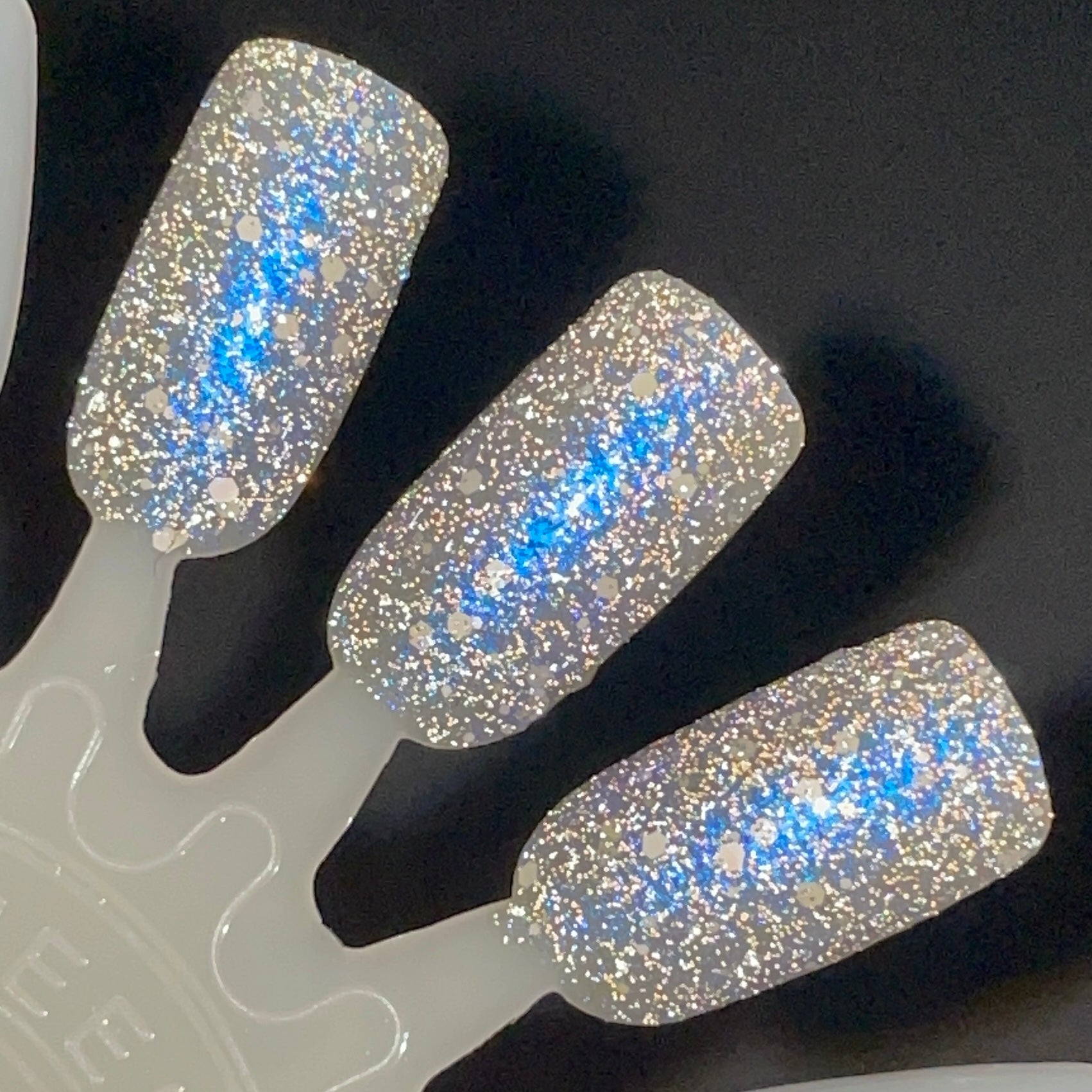 We're Off to See the Blizzard by Dam Nail Polish, dense silver reflective glitter with vivid blue shifting shimmer and scattered white holographic particles under direct flash, swatch stick