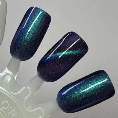 Wake Me Up Before You Cocoa by Dam Nail Polish, deep indigo-purple base with strong cat-eye magnetic pull pattern shifting teal to blue, swatch stick