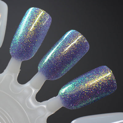 Decade of Dam by Dam Nail Polish, periwinkle-blue base with multichrome gold, green, and teal shimmer and purple reflective glitter particles, swatch stick