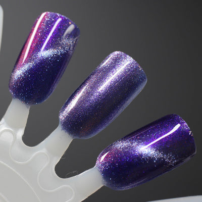 Grand Celebration by Dam Nail Polish, deep violet-purple shimmer magnetic mid-shift from pink-magenta to lavender with silver holographic micro-shimmer, swatch stick