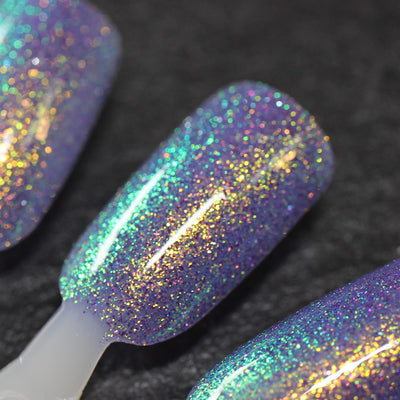 Decade of Dam by Dam Nail Polish, muted periwinkle base showing gold-green-teal shimmer shift with scattered purple reflective glitter, swatch stick