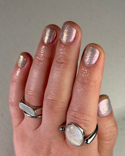 Lavender Haze by Glitch Lacquer on five squoval nails worn with a black lace cuff, very light purple polish with pink multichrome shift and red reflective glitters, light-medium skin tone, bright daylight.