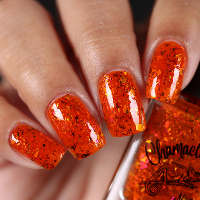 Sauron's Eye by Chamaeleon Nails, red-orange jelly showing gold iridescent flakie flash and copper-to-green ultrachrome shards, on a light-medium skin tone hand