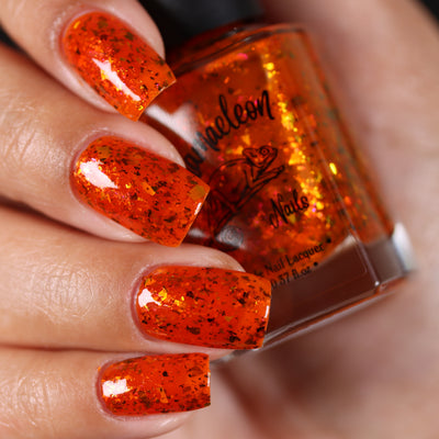 Sauron's Eye by Chamaeleon Nails, fiery orange-red jelly with copper-to-green UCC flakies and iridescent particles, on a light-medium skin tone hand