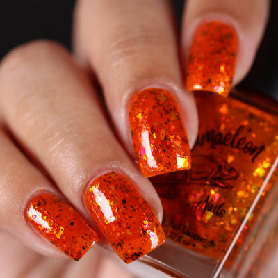 Sauron's Eye by Chamaeleon Nails, orange-red jelly with copper-to-green UCC flakies and pink iridescent flash, on a light-medium skin tone hand