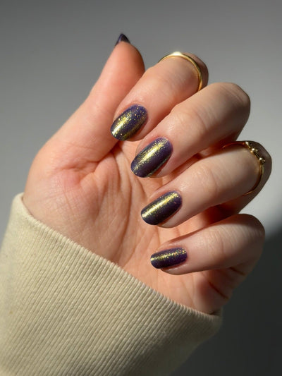 Sandman by Dam Nail Polish, deep blurple jelly with dramatic linear gold-to-green shimmer streak, on a light skin tone hand
