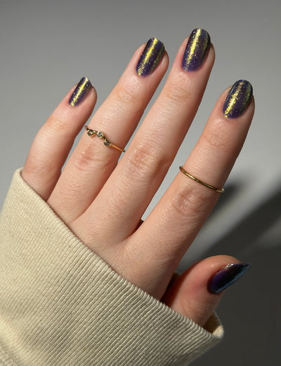 Sandman by Dam Nail Polish, deep blurple jelly with magnetic-style linear gold-to-green shifting shimmer streaks, on a light skin tone hand