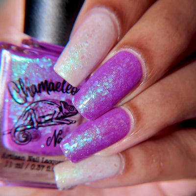Purple Moon (UV Polish) by Chamaeleon Nails, white-to-purple UV multichrome flakie showing mid-shift from creamy white to vibrant violet across nails, bottle held in a light-medium hand