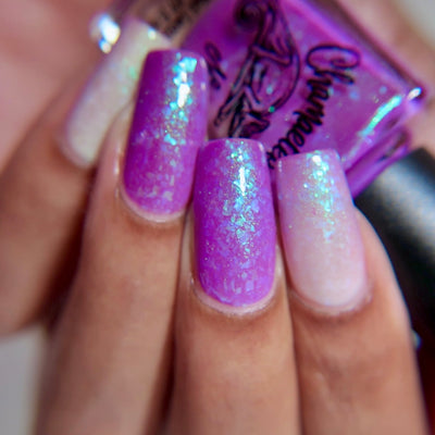 Purple Moon (UV Polish) by Chamaeleon Nails, UV-activated violet-purple jelly with blue-green-turquoise multichrome flakies, gradient from vivid purple at base to sheer blush-white at tips, on a light-medium skin tone hand