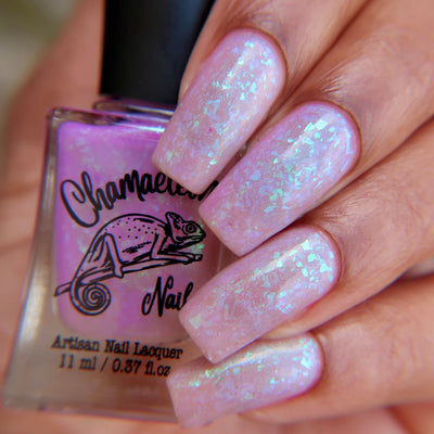 Purple Moon (UV Polish) by Chamaeleon Nails, soft lilac-pink UV-activated base with dense iridescent green-to-teal multichrome flakie shift, bottle held in a light-medium hand