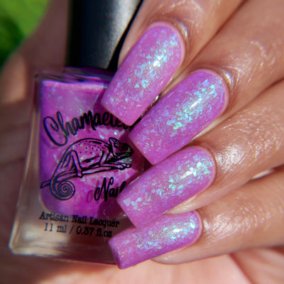 Purple Moon (UV Polish) by Chamaeleon Nails, orchid purple UV-activated jelly with green-to-blue-to-teal multichrome shimmer flakies, bottle held in a light-medium hand