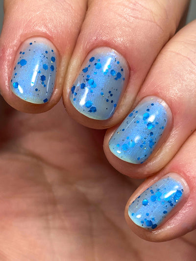 Blueberry Sanctuary by Dam Nail Polish, milky light blue holographic shimmer crelly with assorted metallic blue hex glitters and blue-to-purple shifting shimmer in daylight, on a light-medium skin tone hand