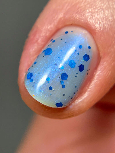Blueberry Sanctuary by Dam Nail Polish, sheer icy pale blue crelly with assorted royal blue hex glitters and fine blue-shifting holographic shimmer dusting, on a light skin tone hand