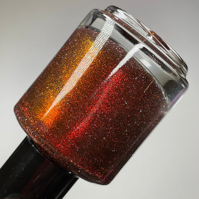 I'm Not Smart Enough by Dam Nail Polish, deep red base with red-to-orange multichrome shimmer and reflective glitter sparkle, bottle standalone product shot