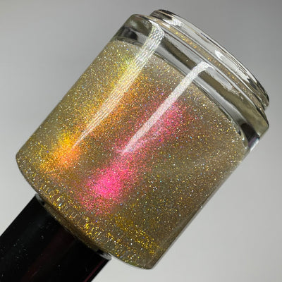 I Love Oklahoma by Dam Nail Polish, gold-green holographic shimmer glitter with vivid red-to-gold-to-pink multichrome shift and linear holo sparkle, bottle standalone product shot