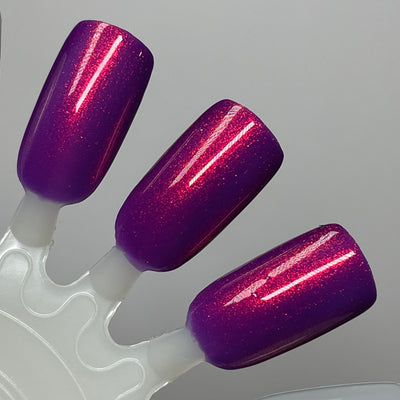 Dark Eyes Blossom by Dam Nail Polish, deep violet-purple shimmer showing duochrome red-to-orange shifting particles under studio lighting, swatch stick