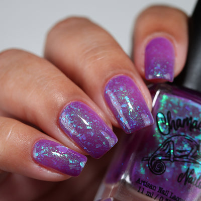 Purple Moon (UV Polish) by Chamaeleon Nails, UV-activated vibrant purple jelly with large teal-to-green multichrome flakies and fine green shimmer, on a light-medium skin tone hand