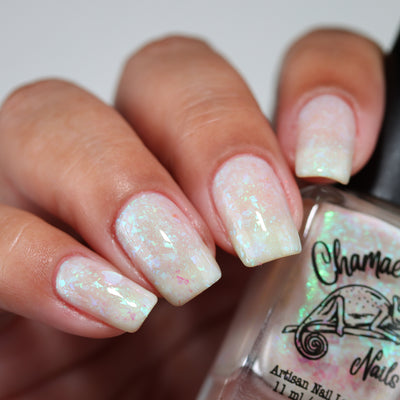 Purple Moon (UV Polish) by Chamaeleon Nails, creamy white resting state with multichrome flakies shifting green, turquoise, and pink, on a light-medium skin tone hand