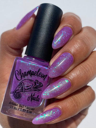 Purple Moon (UV Polish) by Chamaeleon Nails, UV-activated medium violet-purple jelly with green-to-turquoise-to-blue multichrome flakies and green shimmer, bottle held in a medium hand