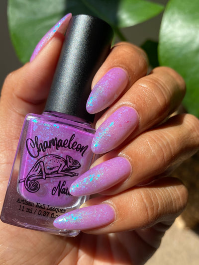 Purple Moon (UV Polish) by Chamaeleon Nails, soft lilac-purple UV-activated base with teal-to-blue iridescent flakie shift and shimmer, bottle held in a medium hand