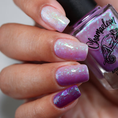 Purple Moon (UV Polish) by Chamaeleon Nails, full UV gradient from sheer milky pink-white to deep violet-purple across four nails with large green-teal-blue flakie shards, bottle held in a light-medium hand
