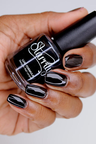 Immortal Jelly by Starrily, glossy black jelly with navy-black depth visible through sheer buildup, bottle held in a medium-deep skin tone hand