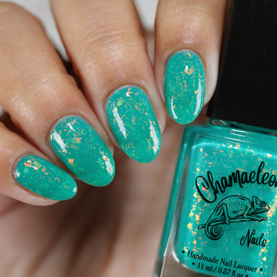Kuang Si Falls by Chamaeleon Nails, vivid neon teal jelly base packed with orange, gold, and yellow iridescent flakies, on a light-medium skin tone hand