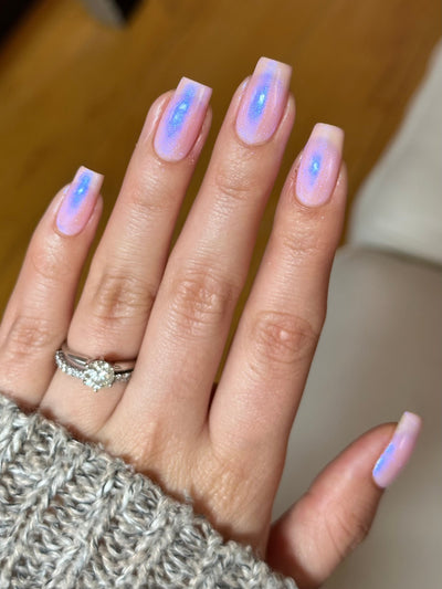 A Whimsical Dream by Dam Nail Polish, sheer pink base with opalescent blurple shimmer pooling and shifting across nail surface, on a light-medium skin tone hand