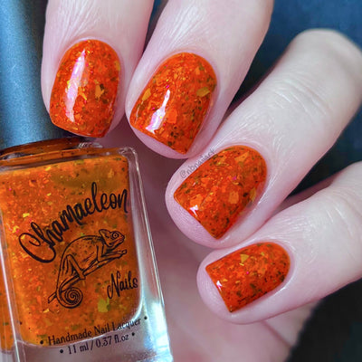 Sauron's Eye by Chamaeleon Nails, fiery orange jelly with flakies shifting pink-to-gold and copper-to-green in bright daylight, on a light skin tone hand