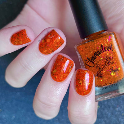 Sauron's Eye by Chamaeleon Nails, fiery orange jelly with multichrome flakies shifting copper to magenta to green in bright daylight, on a light skin tone hand