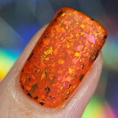 Sauron's Eye by Chamaeleon Nails, fiery orange-red jelly with large copper-to-pink-to-gold UCC flakie shards under direct flash, on a light-medium skin tone hand