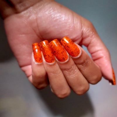 Sauron's Eye by Chamaeleon Nails, fiery orange jelly with dark copper and iridescent ultrachrome flakies under warm indoor light, on a light-medium skin tone hand