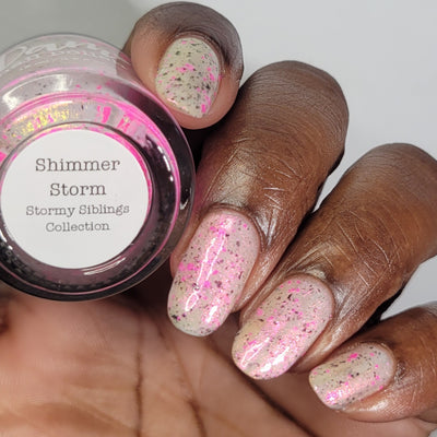 Shimmer Storm by Dam Nail Polish, sheer milky white base with dense neon pink glitter chunks, charcoal-black particles, and pink-gold shimmer, on a rich skin tone hand