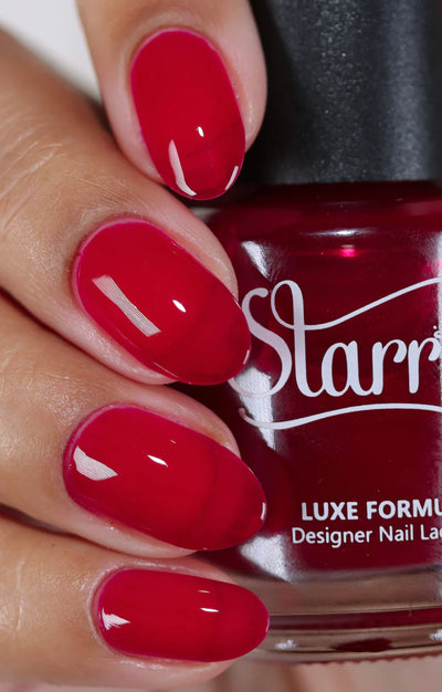 Bloodbelly Jelly by Starrily, vivid crimson red glossy jelly showing brighter tone on nails versus deeper burgundy in bottle, bottle held in a light-medium hand