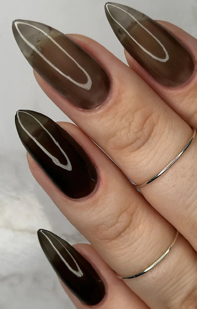 Immortal Jelly by Starrily, black jelly in varying sheer-to-deep opacity, warm brown-black at lighter coats deepening to near-black, on a light skin tone hand