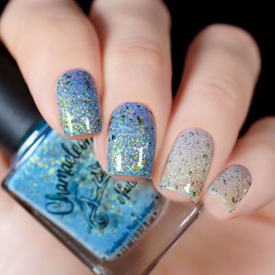 The Forgotten Lagoon (UV Polish) by Chamaeleon Nails, flakie UV mid-shift from periwinkle blue on index and middle fingers to near-white lavender on ring and pinky, with green-gold iridescent and UCC flakes, bottle held in a light hand