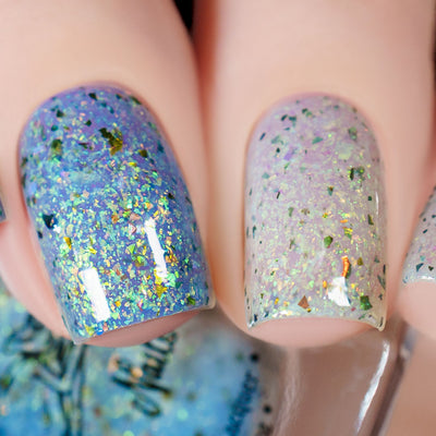 The Forgotten Lagoon (UV Polish) by Chamaeleon Nails, flakie UV with periwinkle-lavender UV-activated half contrasted against sheer white-lavender resting state, green-to-gold and orange iridescent flakes, on a light skin tone hand