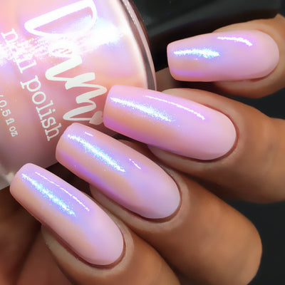 A Whimsical Dream by Dam Nail Polish, sheer soft pink base with bright blue-purple iridescent shimmer streaks under studio light, on a medium-deep skin tone hand