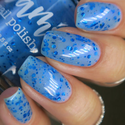 Blueberry Sanctuary by Dam Nail Polish, sheer light blue crelly loaded with vivid metallic blue glitters from fine dots to chunky shards and holographic micro-glitter, on a light-medium skin tone hand