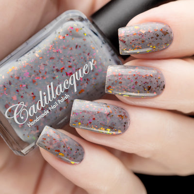 Cadillacquer Daydreaming grey red chameleon iridescent crelly nail polish, bottle held with four-nail swatch, light skin, studio lighting