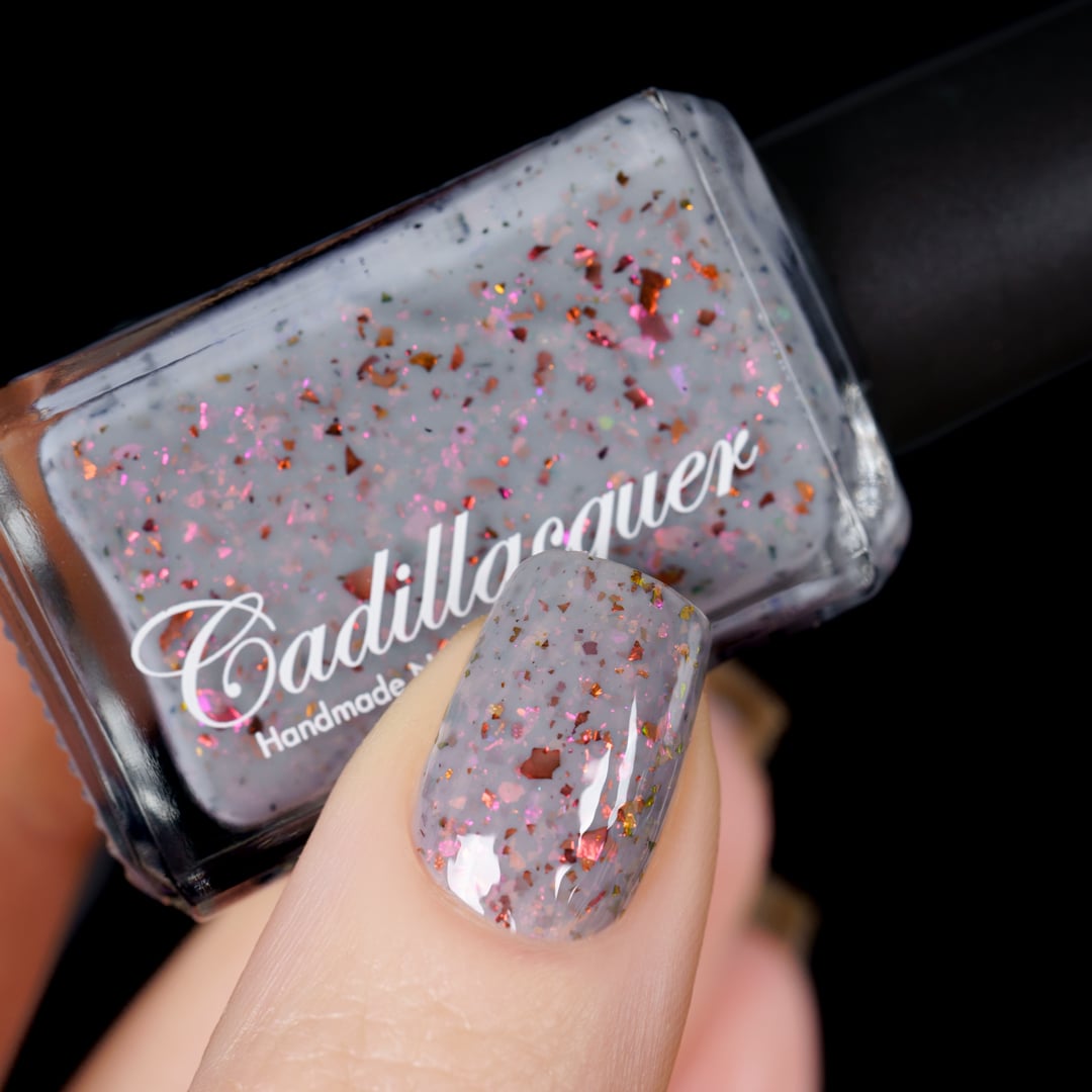 Cadillacquer Daydreaming grey red chameleon iridescent crelly nail polish, bottle held with one-nail swatch, light skin, studio lighting
