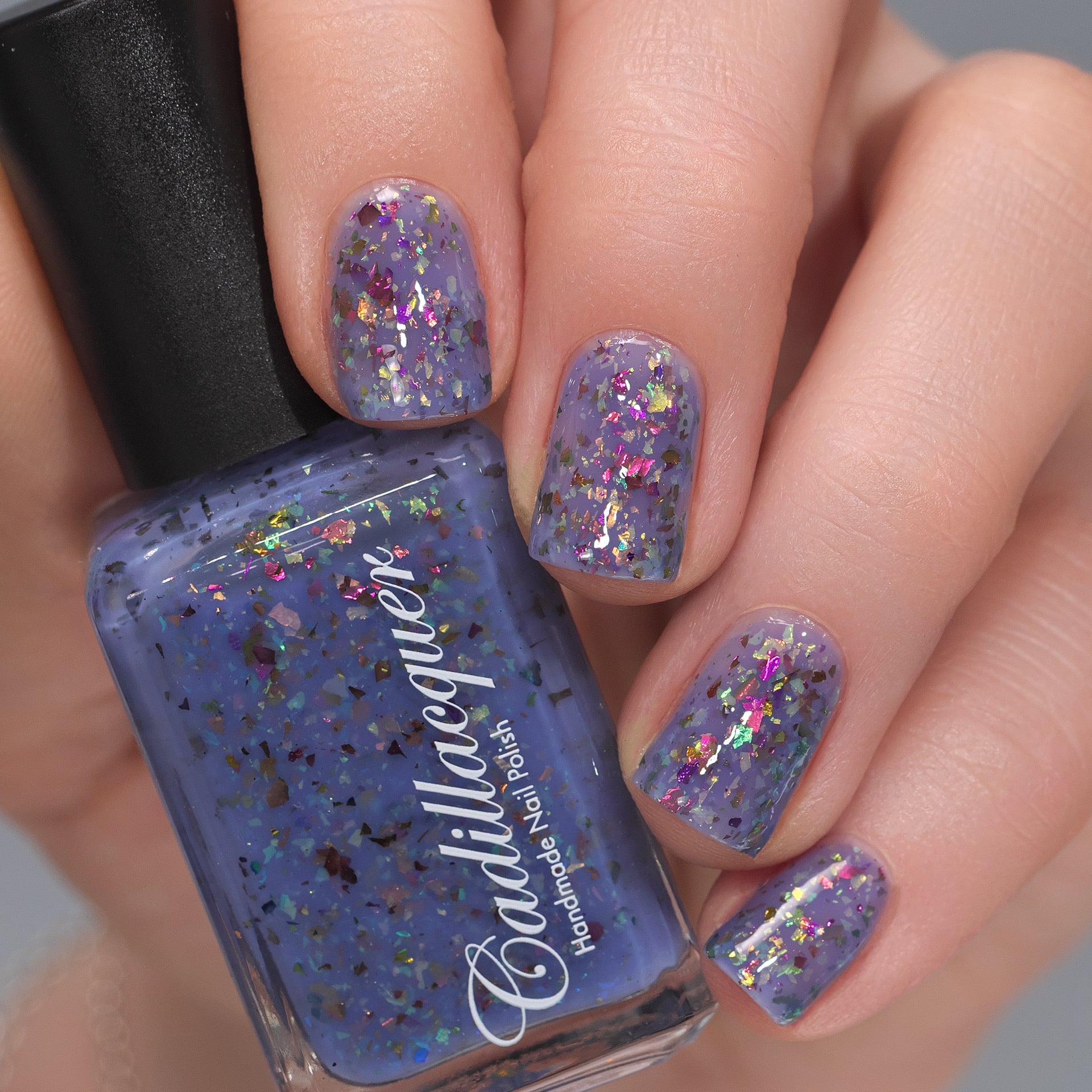 Cadillacquer Don't Worry purple pink chameleon iridescent crelly nail polish, bottle held with four-nail swatch, light skin, studio lighting