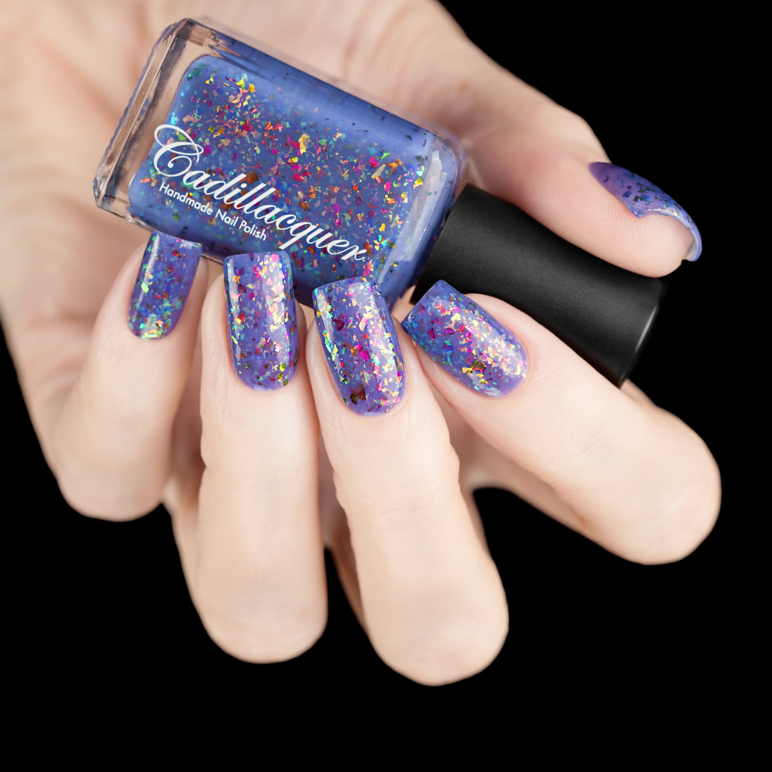 Cadillacquer Don't Worry purple pink chameleon iridescent crelly nail polish, bottle held with five-nail swatch, light skin, studio lighting
