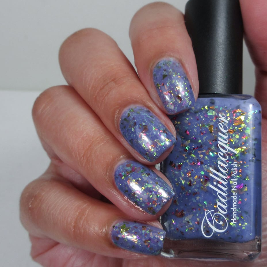 Cadillacquer Don't Worry purple pink chameleon iridescent crelly nail polish, bottle held with four-nail swatch, light skin, studio lighting