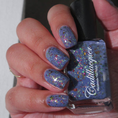 Cadillacquer Don't Worry purple pink chameleon iridescent crelly nail polish, bottle held with five-nail swatch, light skin, bright daylight lighting